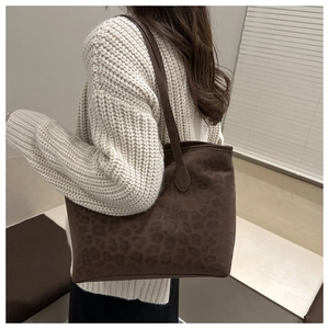 Close-up of brown leopard print suede tote bag worn by model in warm indoor setting