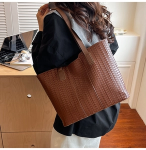 Detail of a large brown woven leather tote bag shown on shoulder for daily commuting