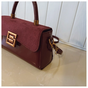 Detail of burgundy textured leather handbag with suede flap and gold S-shaped buckle