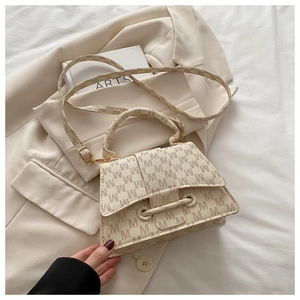 Detail of cream letter print handbag with gold hardware on a beige blazer background