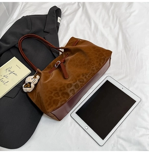 Detail view of large leopard print tote bag with plush charm and smooth brown leather straps