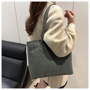 Detail view of large dark grey leopard print tote bag worn with a beige cashmere coat