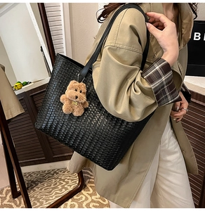 Detail of black woven leather tote bag with a brown plush teddy bear charm accessory