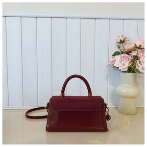 Detail of burgundy matte and glossy leather handbag with gold hardware on table