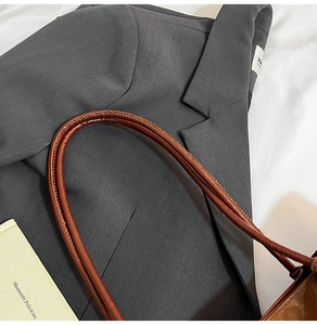 Close-up detail of reinforced dark brown leather handles on a large stylish tote bag