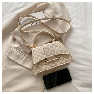 Flat lay of a beige letter-print crossbody bag next to a smartphone and a book