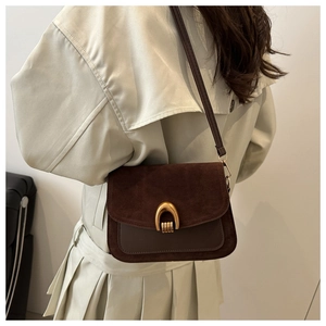 Detail of a brown suede saddle bag with horseshoe gold buckle on a beige trench coat