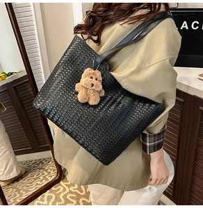 Close-up of black woven leather tote bag featuring a cute brown plush bear charm detail
