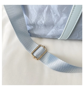Close-up of light blue pleated travel bag with nylon strap and golden metal buckle detail