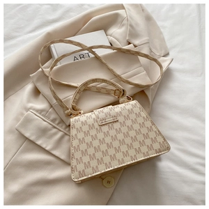 Close-up detail of cream beige tote bag with M-letter pattern and gold-tone hardware