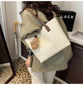 Macro detail of cream woven tote bag with brown leather strap and teddy charm