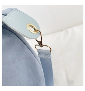 Detail of light blue travel bag showing golden metal hook and wrinkled fabric texture