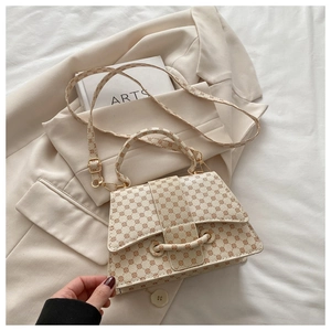 Detailed view of beige monogram handbag with golden buckles on a minimalist background