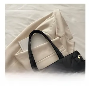 Detail of black quilted tote bag with textile handles and gold zipper on a beige blazer