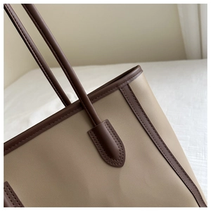 Detail of reinforced deep brown leather handle stitching on the beige tote bag