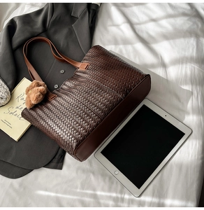 Detail of dark brown woven tote bag with slim handles and a cute plush bear charm