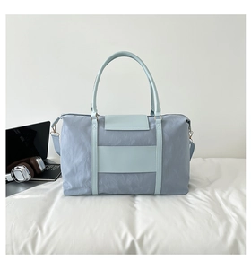 Light blue nylon travel bag with gold hardware shown on a desk with laptop accessories