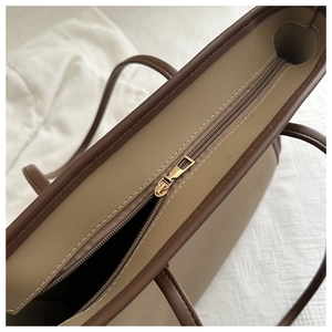 Detail of metal zipper closure and brown trim on a khaki faux leather tote bag