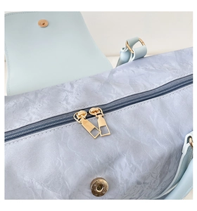 Detail of light blue wrinkled fabric travel bag with gold zippers and magnetic flap closure