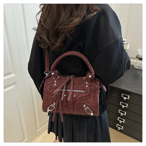 Detail shot of burgundy suede handbag featuring silver studs and long leather tassels