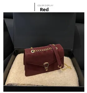 Close-up of wine red chain bag with gold buckle on soft knit fabric inside a black box
