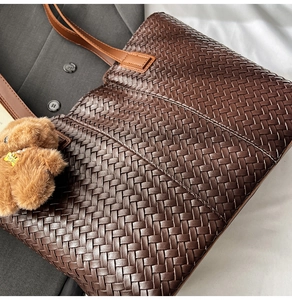 Detail of dark brown woven tote bag featuring a plush bear charm on a grey suit jacket