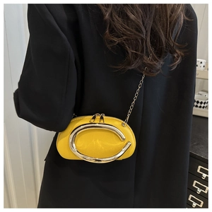 Detail of yellow pebbled leather crossbody bag with silver C-shaped metal hardware and chain