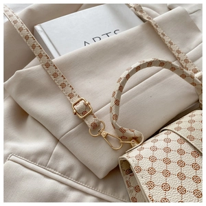 Detailed close-up of cream monogram pattern bag with luxury gold-toned hardware hooks
