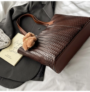 Detail of dark brown woven tote bag with smooth leather strap and cute bear charm
