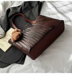 Detail of dark brown woven tote bag with plush ball charm and sleek shoulder straps