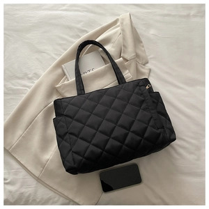 Macro view of black quilted tote bag with diamond stitching on beige blazer background