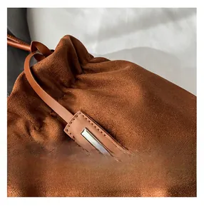 Detail shot of brown suede bucket bag with fine stitching and metal tag ornament
