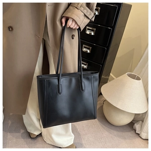 Close-up of minimalist black leather tote bag held by a model in a trench coat