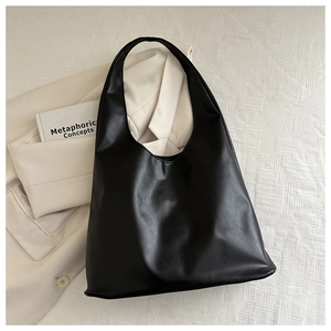 Close-up of a matte black leather tote bag on a neutral beige blazer background