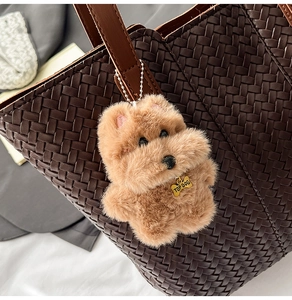 Close-up of a plush dog charm with TOP DOG tag hanging on a woven brown tote bag