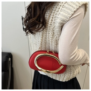 Detail of red leather bag with large gold C-shaped metal handle and elegant chain strap