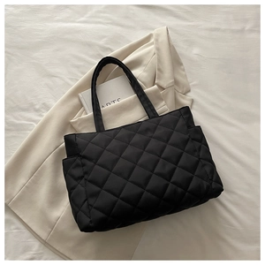 Detail of black quilted tote bag with large diamond stitching and side pocket