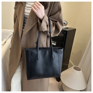 Chic black leather tote bag with long straps styled with a trench coat for work