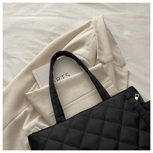 Detail of black quilted tote bag with metallic zipper and elegant diamond stitching pattern
