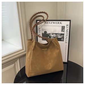 Detail of a brown suede tote bag with woven handles and golden logo on black surface