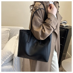 Chic black leather tote bag styled with a khaki trench coat for a modern winter outfit