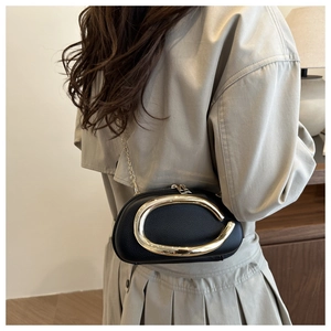 Detail of a chic black oval clutch with gold C-handle and fine chain strap on a model