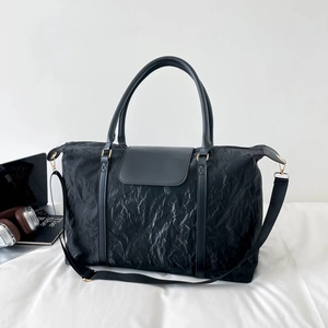Large black travel tote bag with textured pleated fabric and leather handles in lifestyle setting