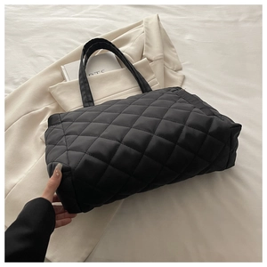 Close-up of the black quilted rhombic pattern on a large tote bag with a wide strap