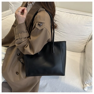 Detail of a large black leather tote bag worn with a khaki trench coat for a stylish look