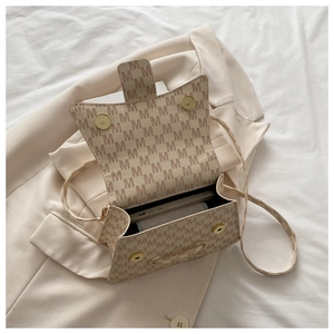Close-up of beige crossbody bag with M letter pattern on a neutral blazer background