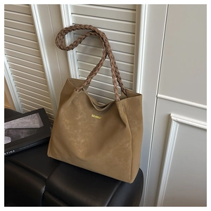 Detail of coffee brown tote bag with thick braided handles and gold logo on leather bench