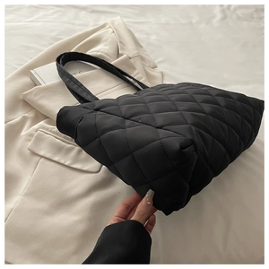 Macro detail of black quilted puffer tote bag showing diamond stitching texture on a suit