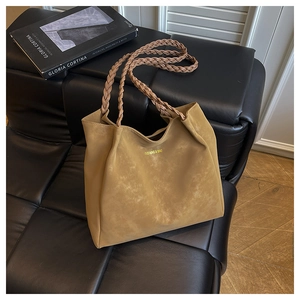 Detail of khaki tote bag with woven handles and brand logo on a black leather sofa