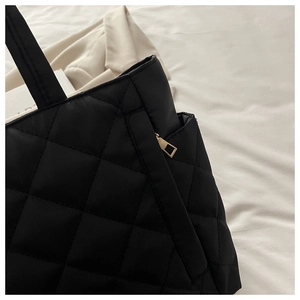 Detailed close-up of black quilted tote bag featuring golden zipper and nylon texture